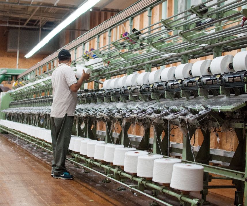 An employee in Sock Club's cotton yarn spinning facility changing out a finished cotton yarn spool in the United States