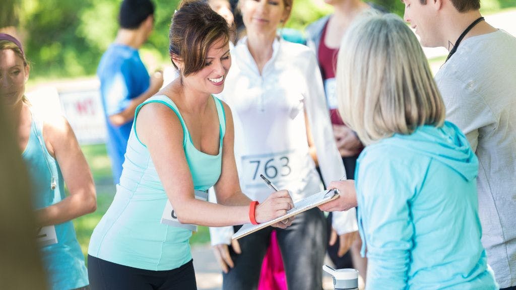 A woman at a 5k event for nonprofit fundraising signing up to give a donation on a clipboard with a sunny park in the background