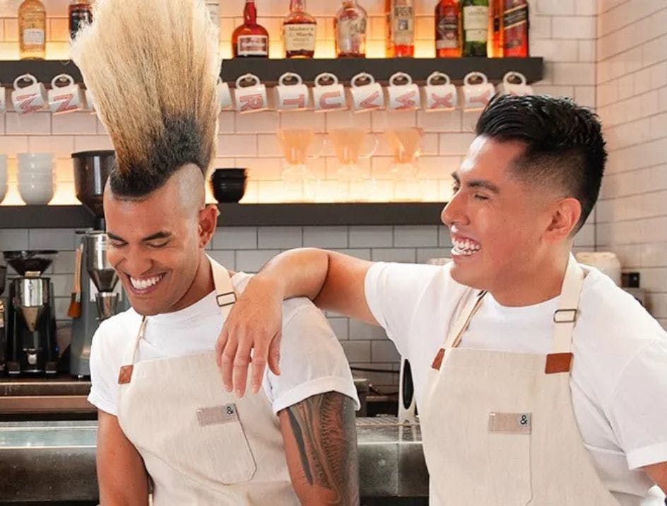 Two chefs in a kitchen at a Kimpton property laughing in a kitchen with their arms around each other