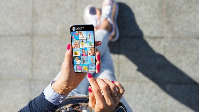 Woman with pink nails shopping for custom merch on social media on her phone outside during the day