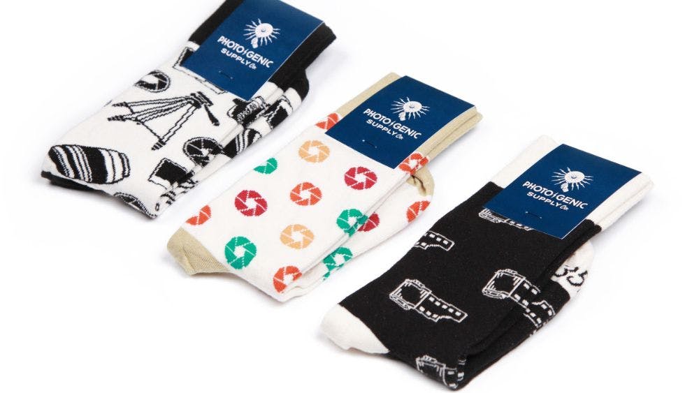 Three different wholesale sock designs for Photogenic Supply on a white background, featuring custom packaging and photography-themed sock designs