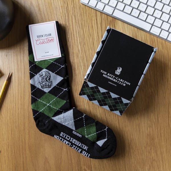 Green and black argyle custom sock next to custom sock box on desk
