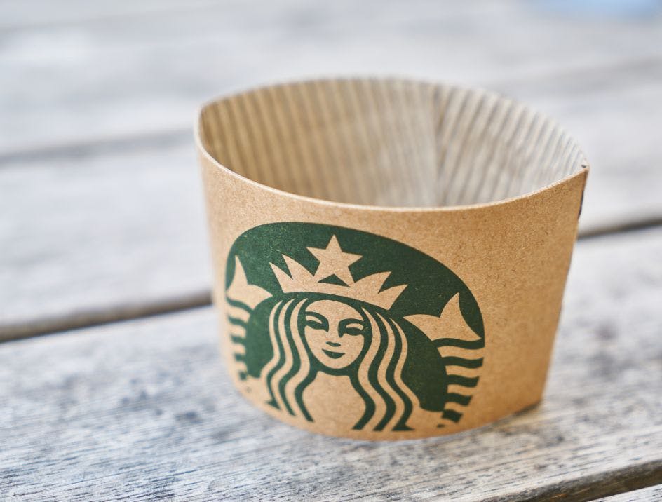 A branded coffee sleeve on a table outside showing the Starbucks logo