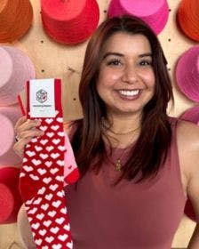 Sock Club Sales team member Rebecca Palomares standing in front of a wall of yarn holding socks