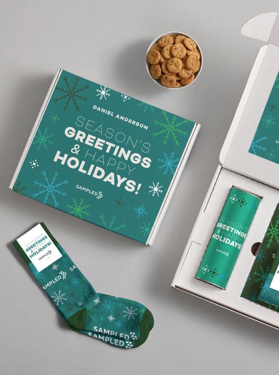 A branded holiday corporate gift kit including custom socks, a branded mailer box, and a custom printed tin of cookies