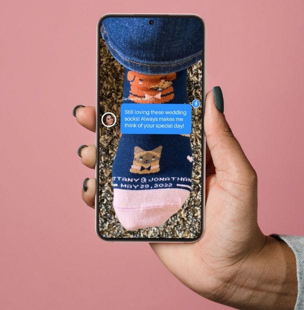 A hand holding up a cell phone displaying a text message from a wedding guest saying how much they love their custom wedding socks