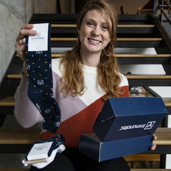 Employee sitting on stairs smiling holding a pair of custom socks