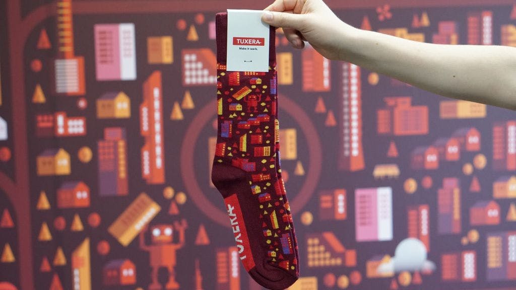 Custom socks for Tuxera being held by an employee's hand in front of a wall that has the same pattern as the sock
