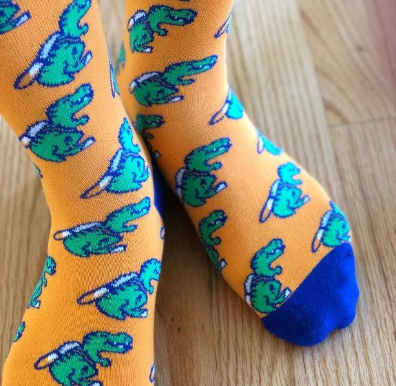 Custom socks that Sock Club made for Rattle that are orange with the Rattle dinosaur mascot knitted into them
