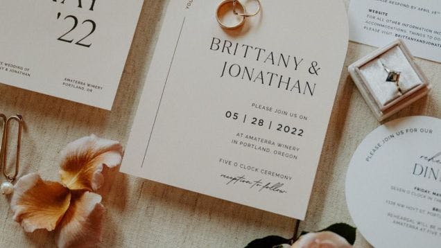 A wedding invitation and wedding rings in peach and cream tones laid out on a table