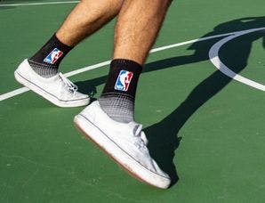 A man playing basketball outside on an outdoor court in custom athletic socks with the NBA logo on them