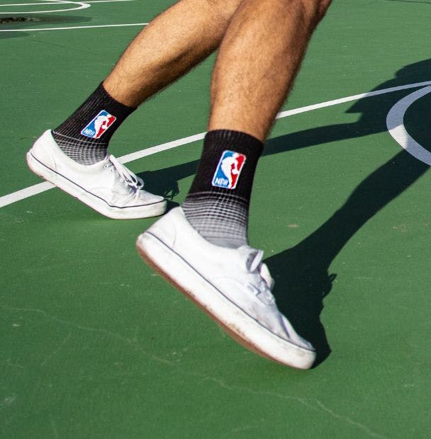 A man playing basketball outside on an outdoor court in custom athletic socks with the NBA logo on them