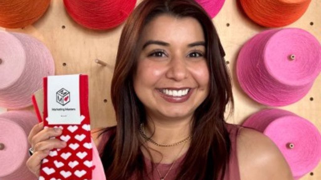 Sock Club Sales team member Rebecca Palomares standing in front of a wall of yarn holding socks