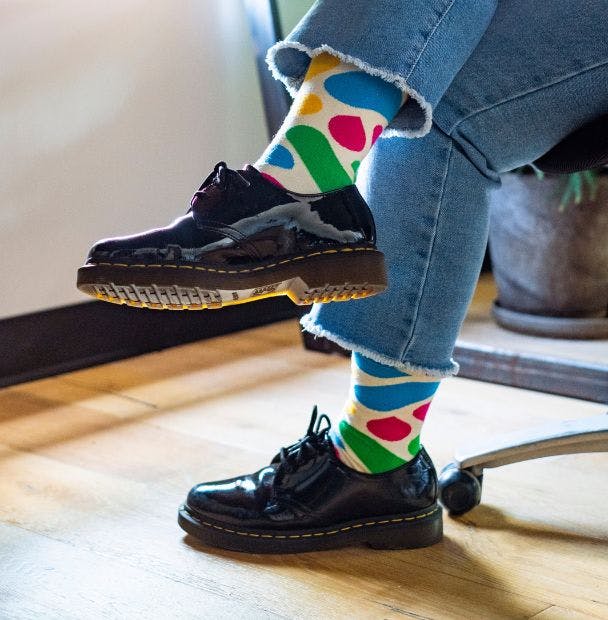 Custom dress socks for Slack worn by an employee in an office sitting in a desk chair with black shoes and jeans