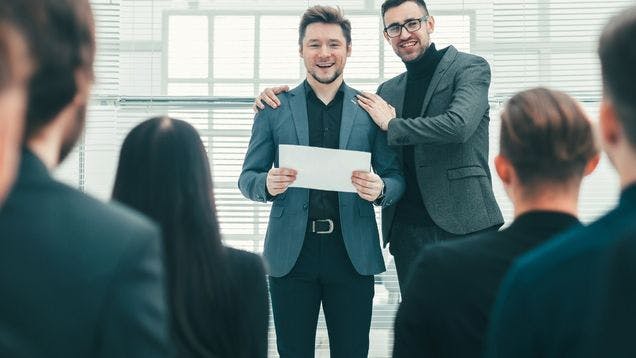 Employee and Boss wearing suits holding Employee Recognition award in a crowded meeting room