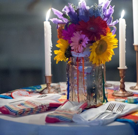 Wedding table setup including rainbow flowers in a vase, lit candles, and custom wedding socks on the table