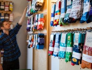 Man hanging socks up in a company store filled with customized socks with logos on them