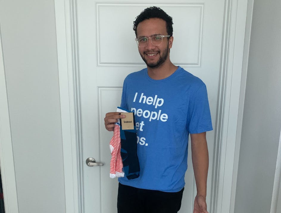 Person smiling and wearing blue custom shirt and holding branded socks from new hire package