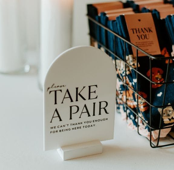 Custom Wedding socks on a white table at a wedding with a sign that encourages wedding guests to take a pair as a wedding favor