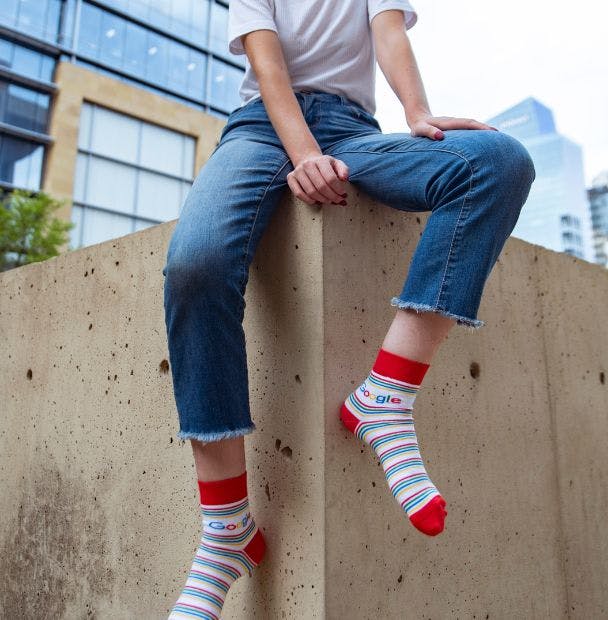 Branded quarter crew socks for Google being worn by a young woman outside sitting on a concrete bench