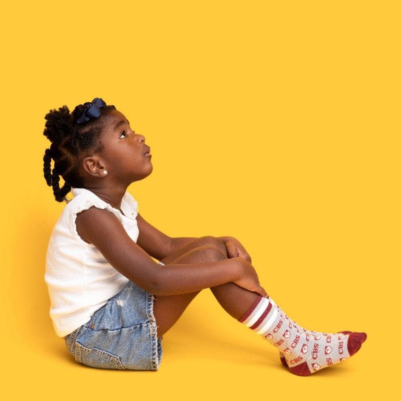 Little girl sitting down in yellow background with custom youth socks on