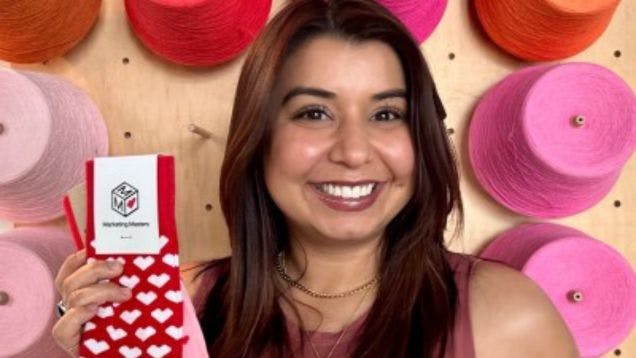 Sock Club Sales team member Rebecca Palomares standing in front of a wall of yarn holding socks