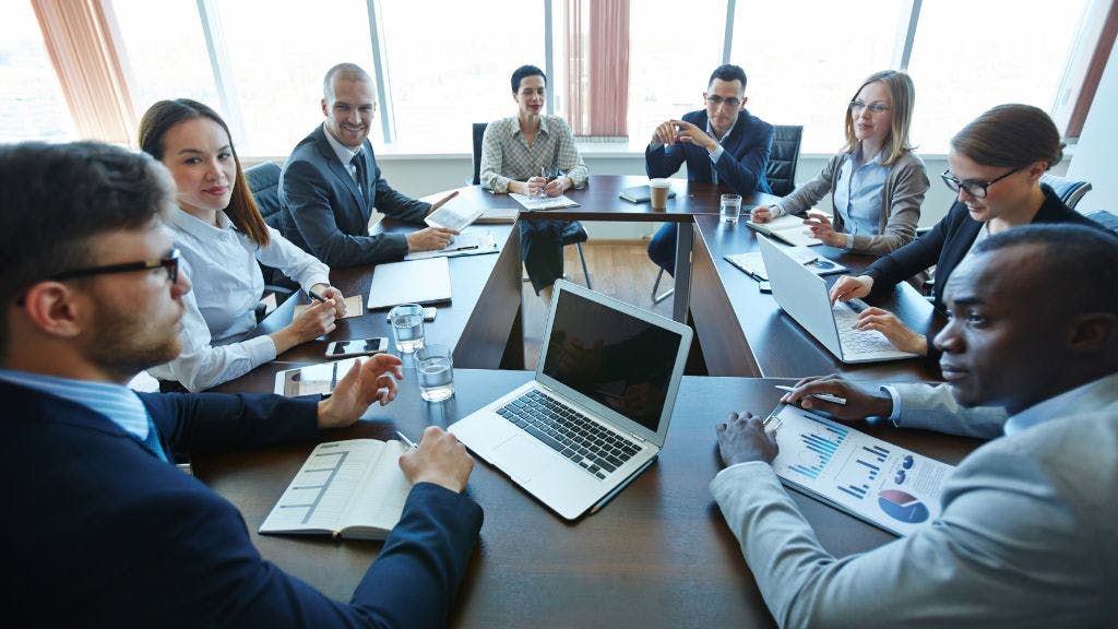 A group of people sitting at desks in a circle at a corporate conference