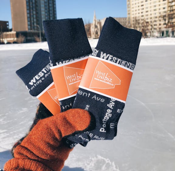 Orange gloved hand holding West End Biz custom logo socks with ice in background