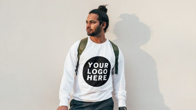 Young cool man wearing a branded sweatshirt posing against a light colored wall