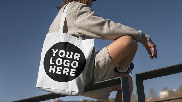 A customer sitting on a fence outside with a tote bag that was created as branded merchandise to create customer loyalty