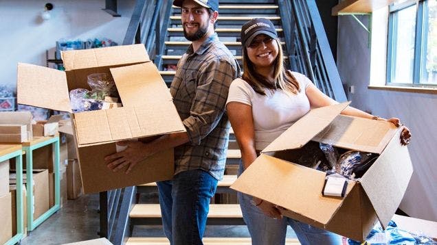 Two Sock Club employees in a warehouse holding boxes bulk fulfilling a custom sock order