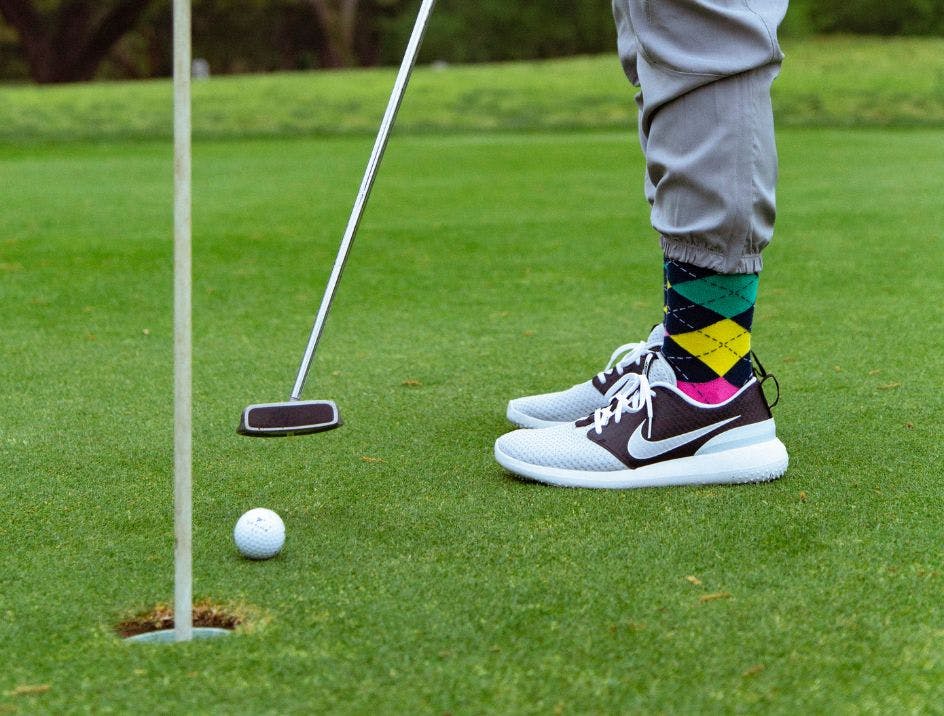 Custom argyle golf socks on a golfer putting into the hole on a green