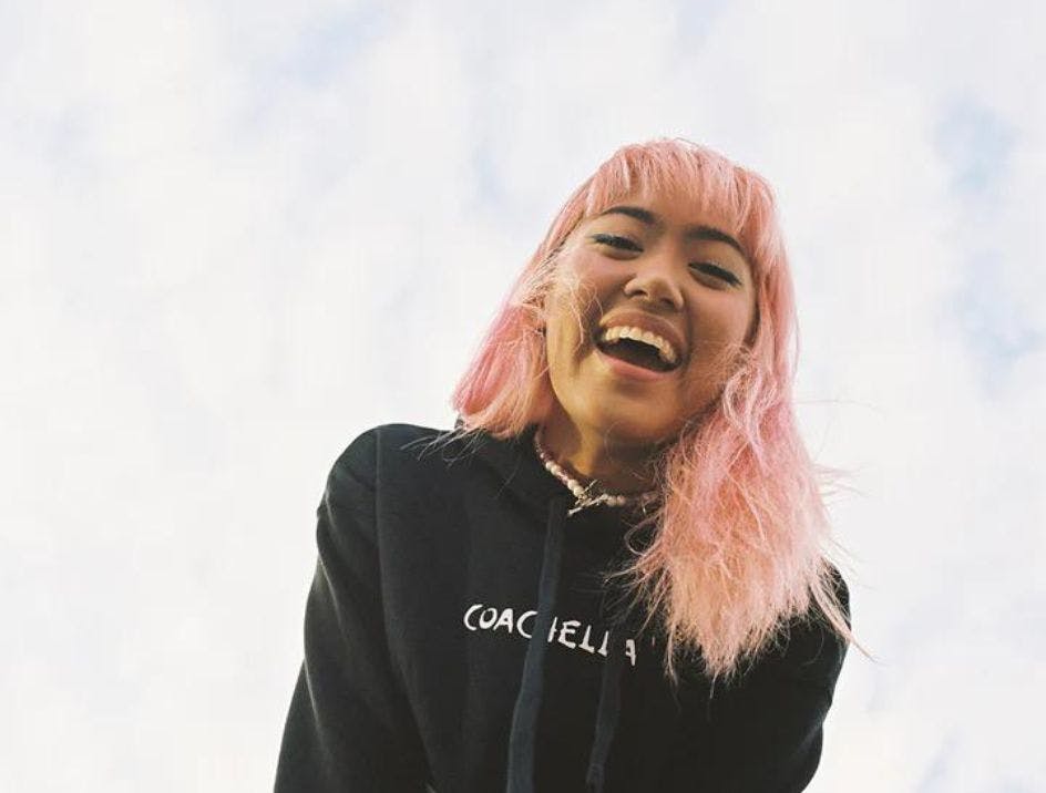 Young woman with pink hair wearing a Coachella branded festival sweatshirt in front of a blue sky