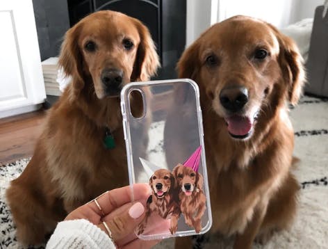 Golden retrievers sitting next to a personalized phone case with their faces on it 