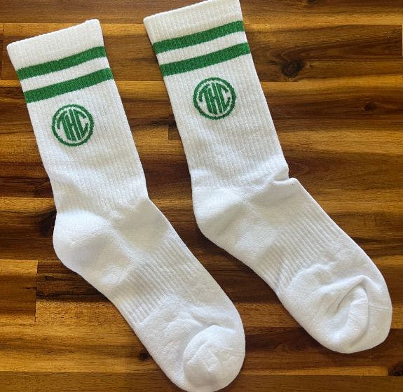 Branded white custom athletic socks for The Herban Cannasseur on a wooden background