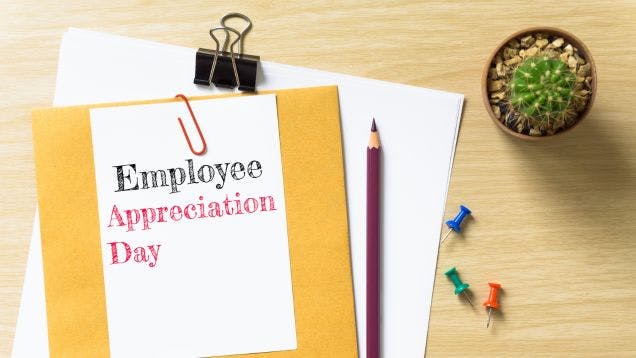 A notebook on a desk showing a sign that says "Employee Appreciation Day" with a pencil and a cactus