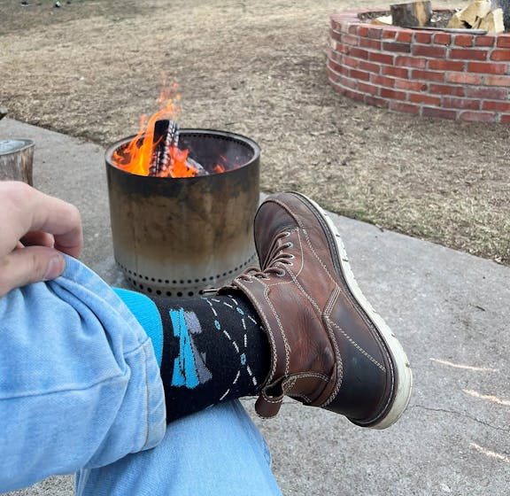 Person wearing black and blue custom logo socks for Harper Turf with fire pit in the background 