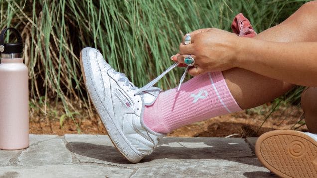 A woman putting on running shoes over custom socks that she got as an employee appreciation gift