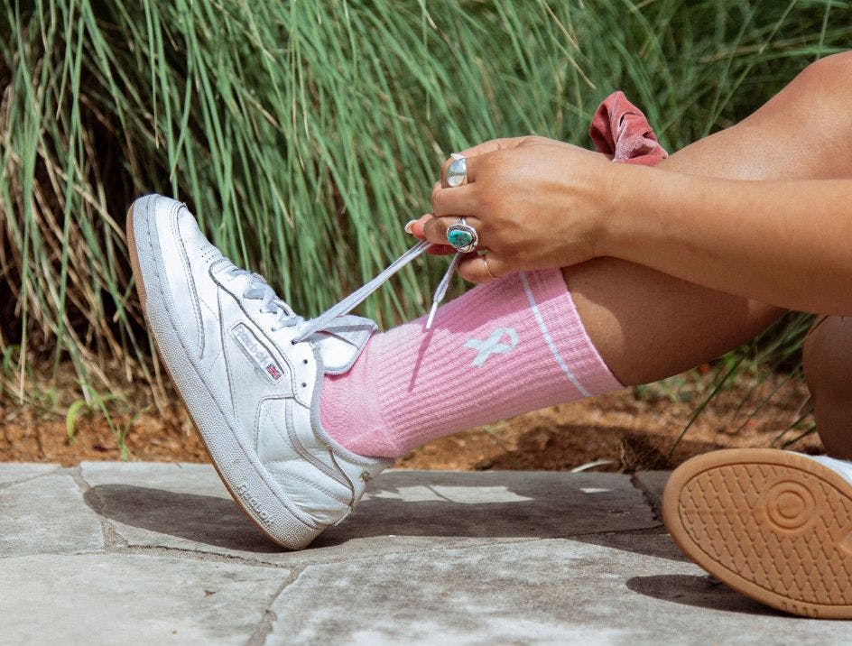 Woman tying the laces on her shoes showing off her pink running socks, getting ready to go for a run outside.