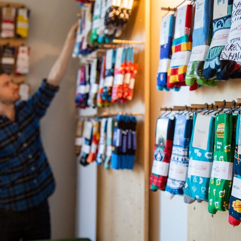 Man hanging socks up in a company store filled with customized socks with logos on them