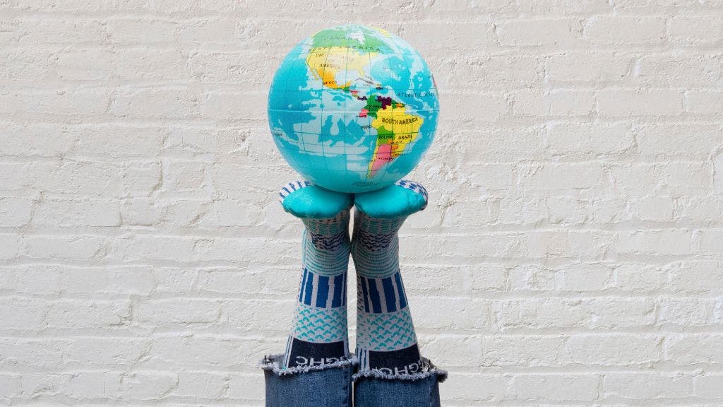 Colorfully patterned custom socks holding up a globe in front of a brick wall