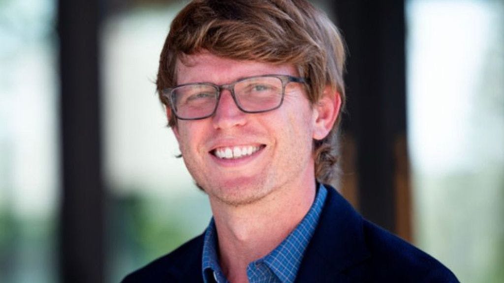 Sock Club Senior Operations Coordinator Hamish Roberts pictured smiling in a blazer in an office setting