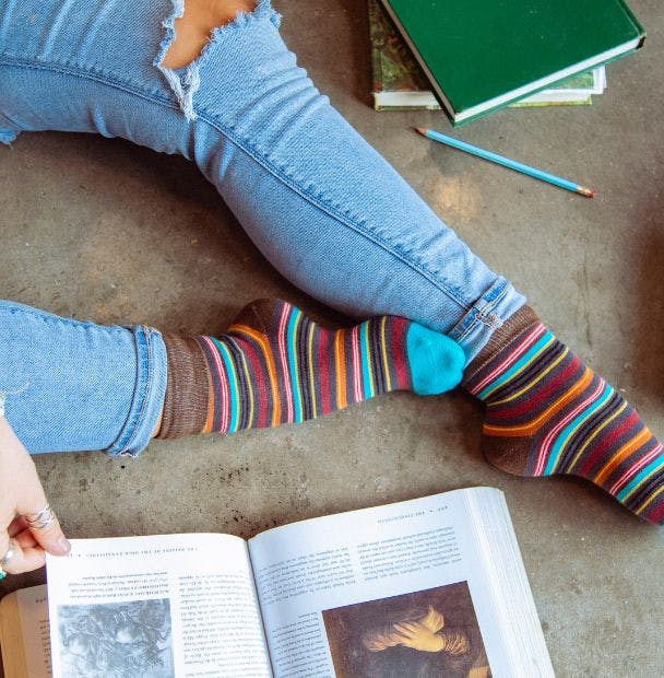 Cheap striped custom socks with logo being worn by a woman reading books on the floor of her home