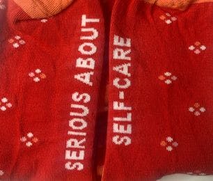Red and orange custom socks with the message "serious about self-care" woven into the soles of the feet of the socks
