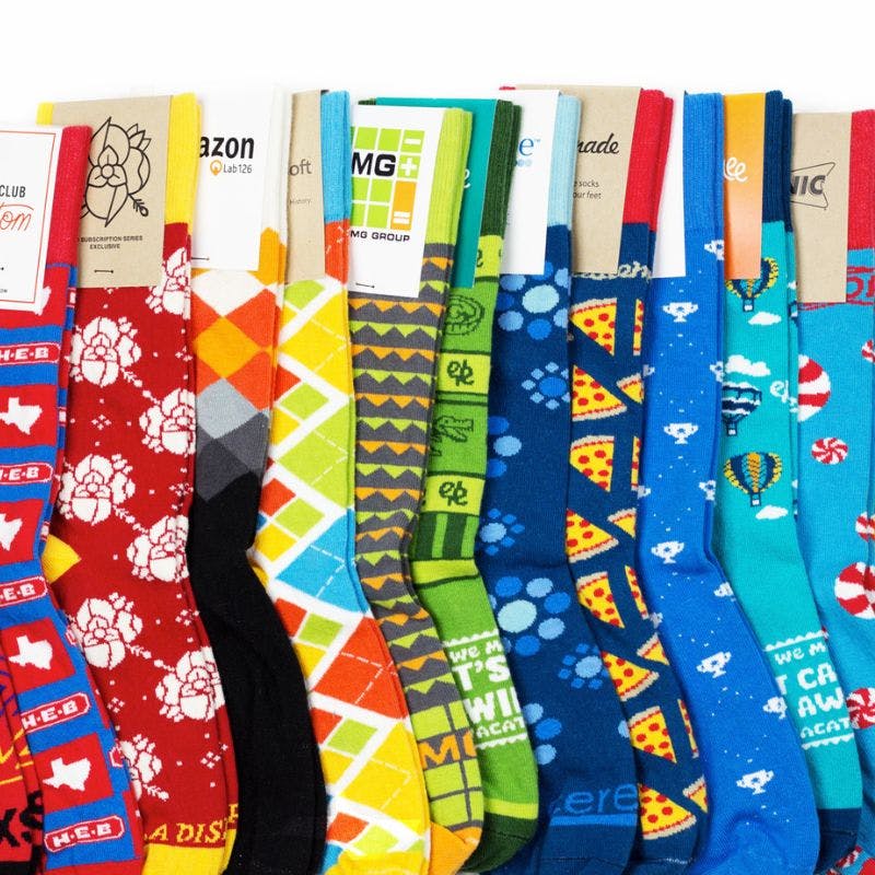 A rainbow of custom socks laid out showcasing different designs for Amazon, Microsoft, Sonic, and more
