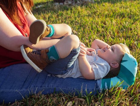 Baby with socks on mom's lap at park grass.