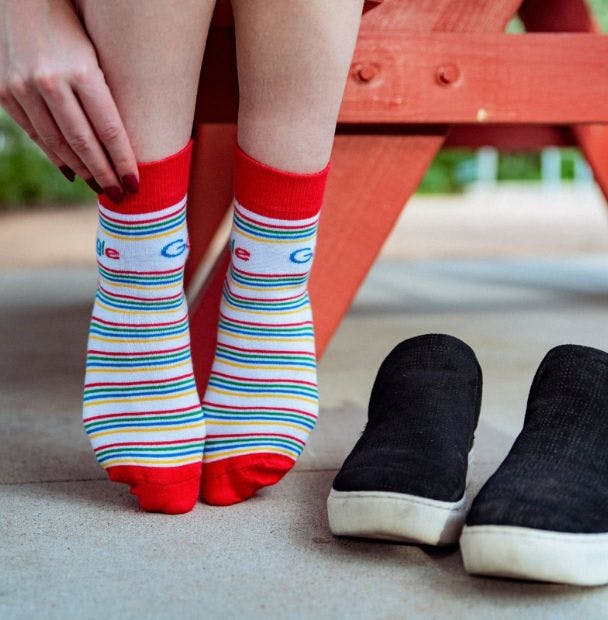 Custom quarter crew socks for Google being worn by a young woman sitting at a picnic table outside