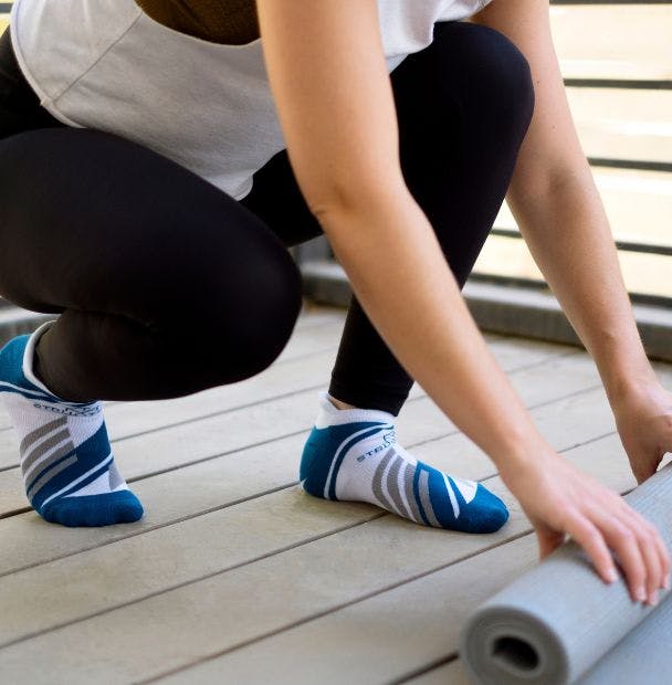 Woman rolling up a yoga mat wearing custom athletic ankle socks with cushion and compression