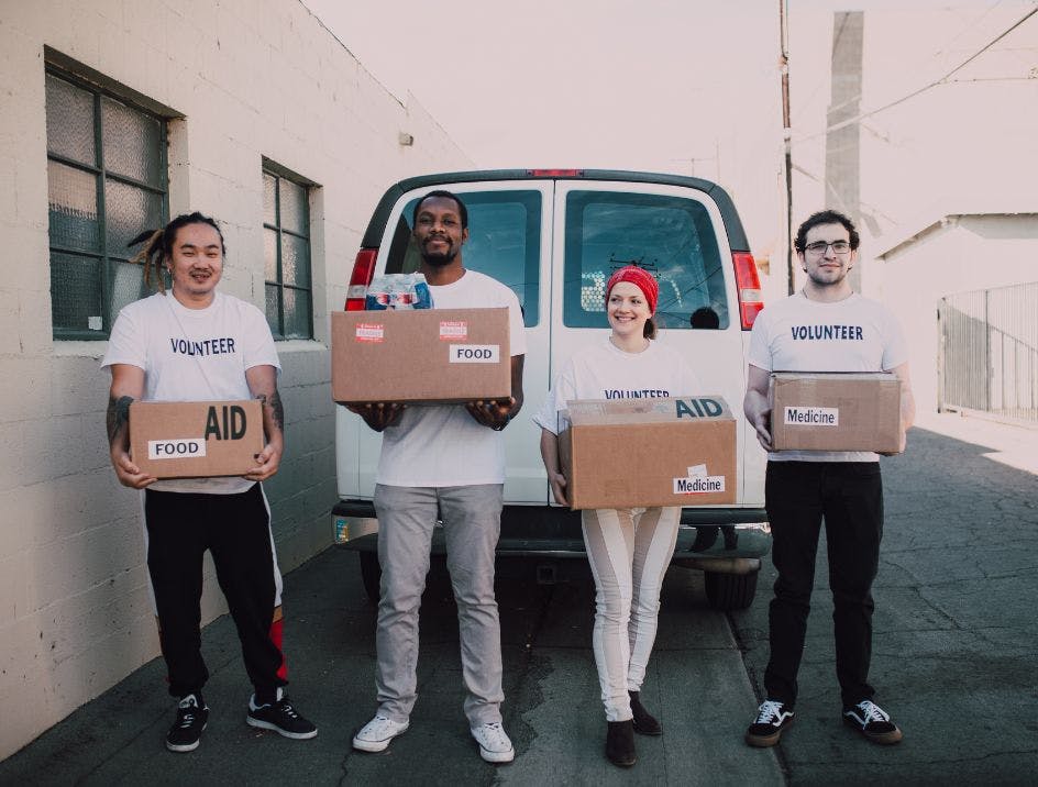 A group of volunteers holding supplies for their nonprofit organization in front of a van used to carry those supplies