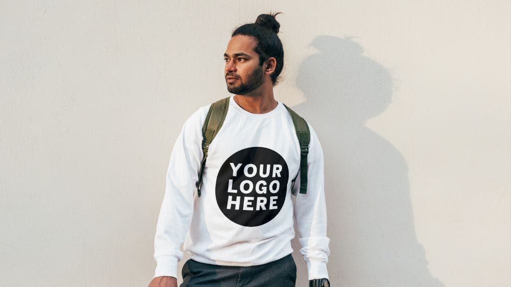 Young cool man wearing a branded sweatshirt posing against a light colored wall